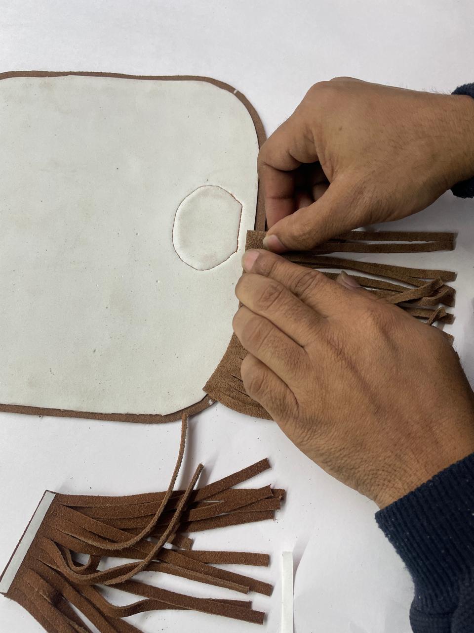 Artisan en train d’assembler et coller des franges en cuir sur une pièce de maroquinerie Charlay Stone, illustrant le savoir-faire de fabrication.